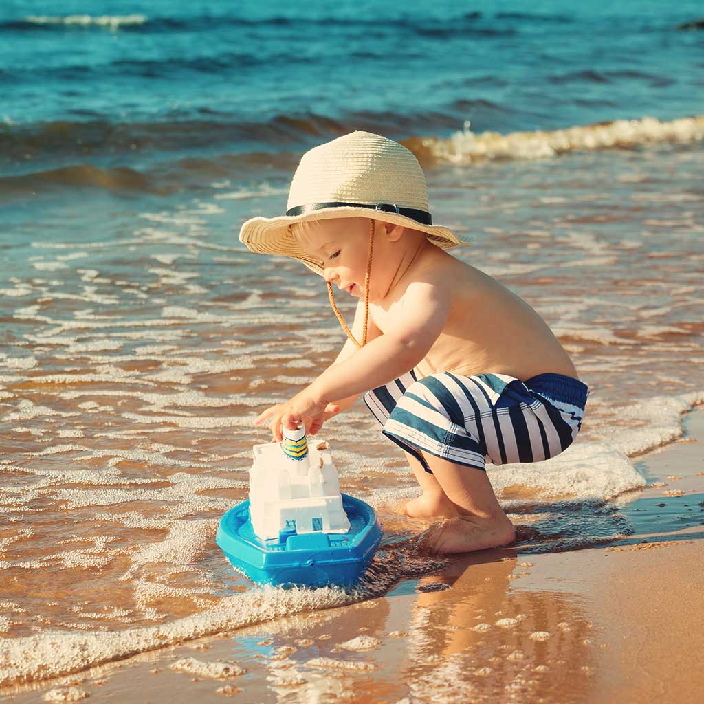 Ein Kleinkind spielt mit einem Plastikboot am Ufer.