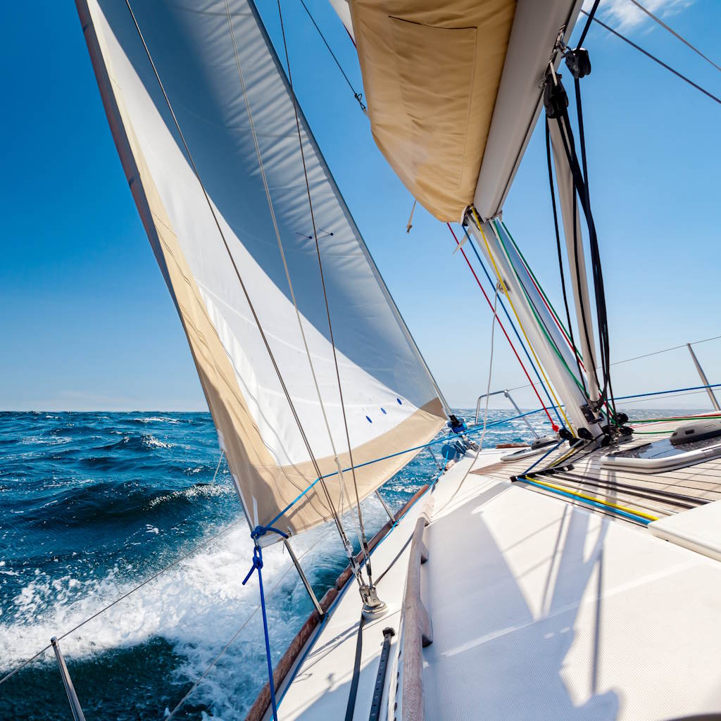 Weißes Segelboot auf offener See vor blauem Himmel.
